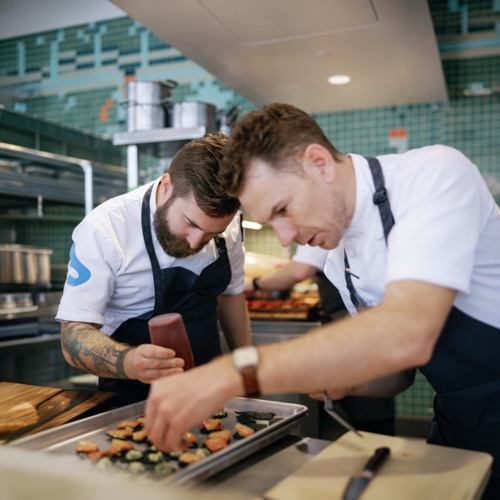 Two Salesforce chefs assembling small dishes together in a commercial kitchen