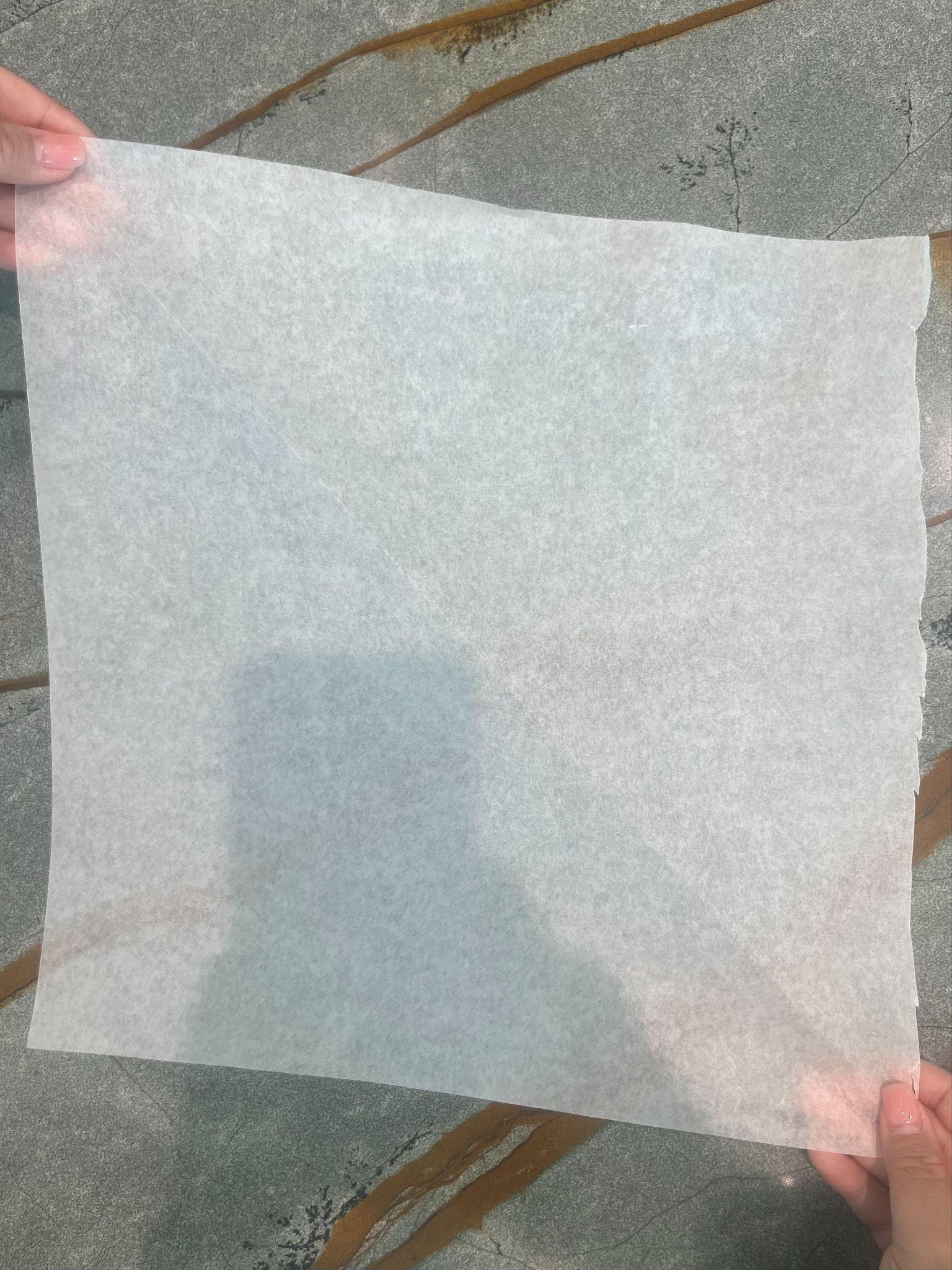 Hands holding a square sheet of parchment paper over a stone counter