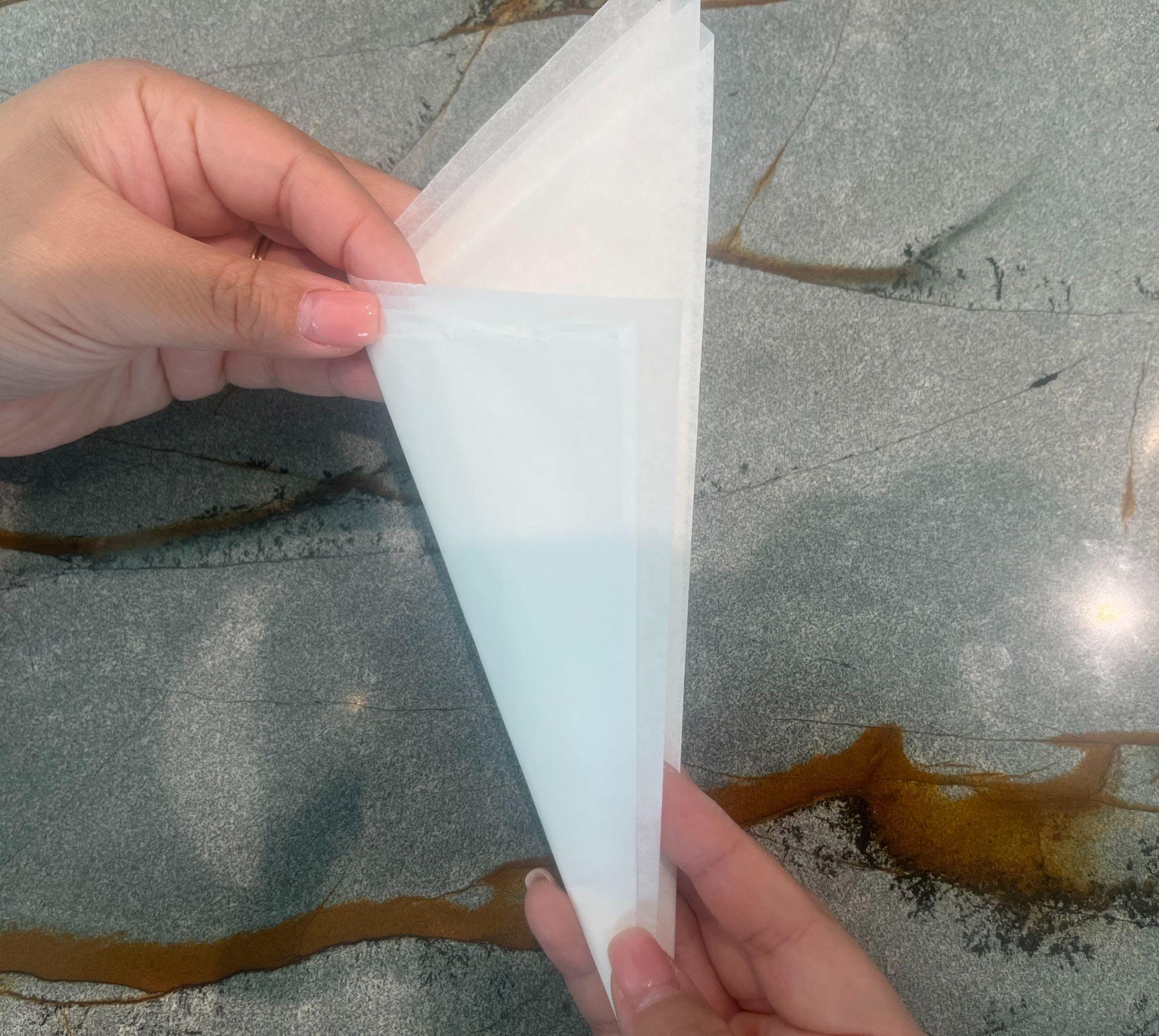 Hands folding the parchment into a narrower irregular triangle