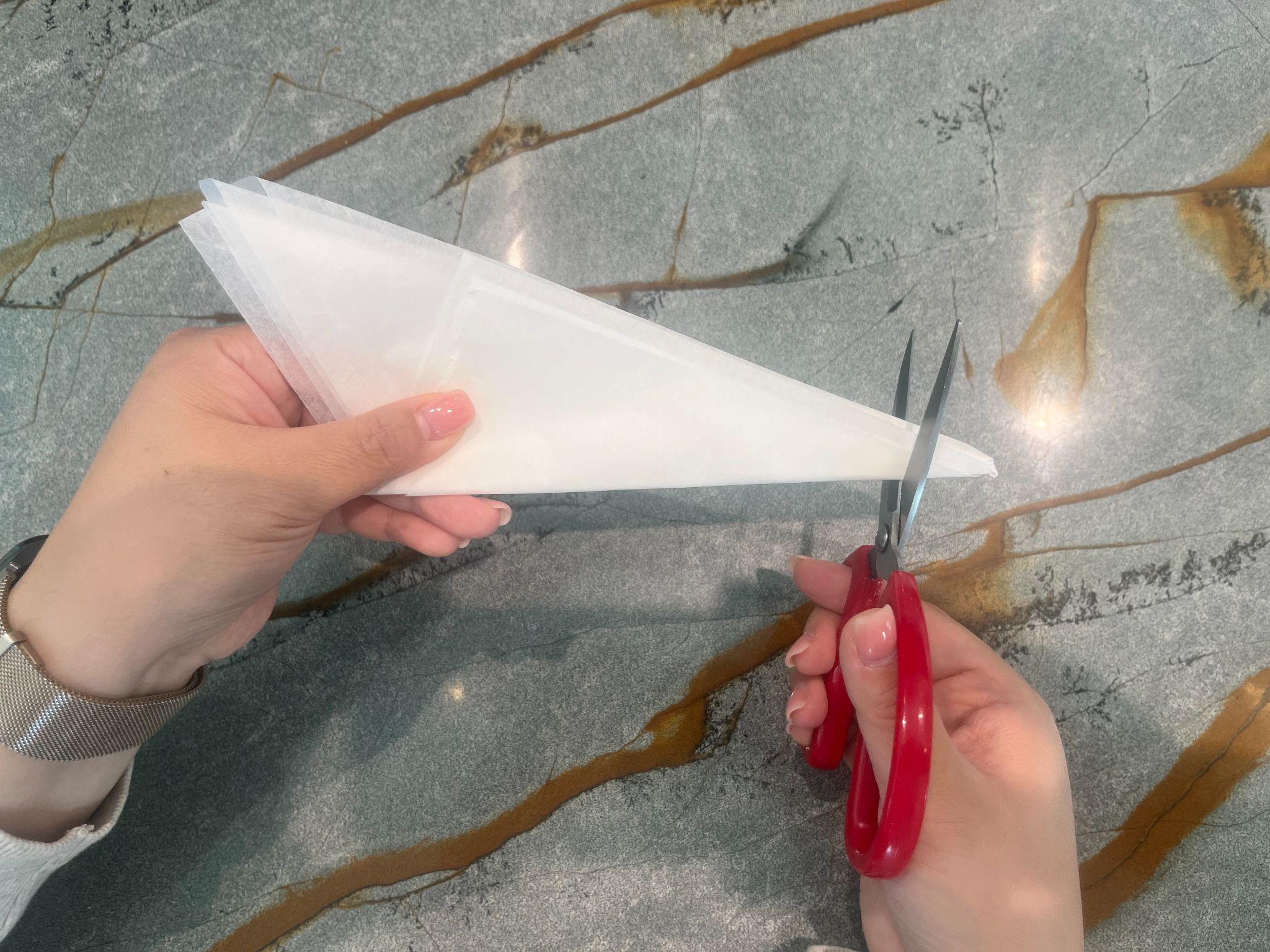 Hands trimming the tip of the folded parchment triangle with red scissors
